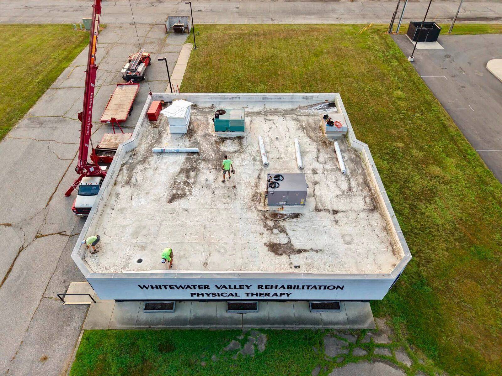 A commercial building in Connersville mid-project, with the roof deck torn off and crew and crane on site.